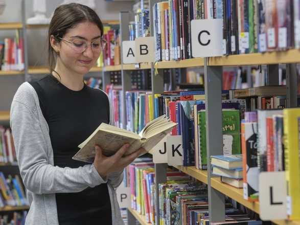 Junge Schülerin blättert in einem Buch in der Bibliothek